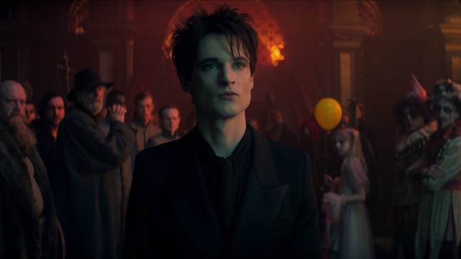 Tom Sturridge as Dream stands in a room full of people in The Sandman.