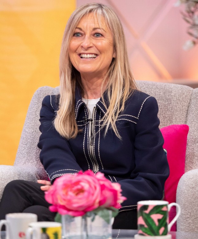 Fiona Phillips with blonde hair and a black blazer sat on the sofa