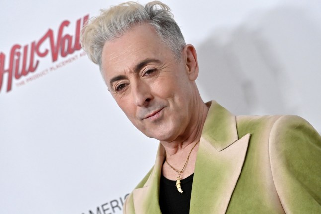 Alan Cumming wearing a green suit and posing on the red carpet.