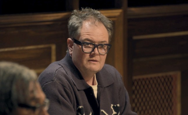 Alan Carr sits wearing glasses as he reacts at the roundtable.
