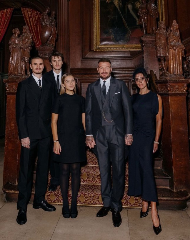 A picture of the Beckhams family, minus Brooklyn, all dressed in black/grey in a dark oak wood room, gathering for Sir David's knighthood.
