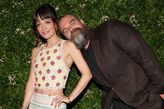 Lily Allen and David Harbour posing for photo in front of hedge.