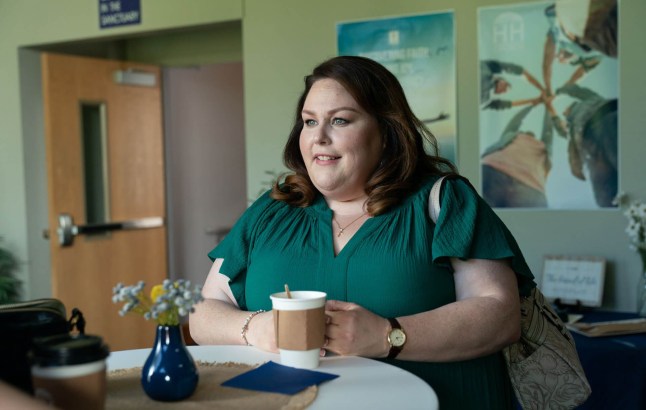 Woman in green top sits holding a cup of coffee in the Hunting Wives.