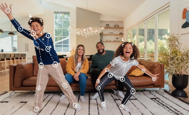 Two kids in a living room moving while playing a video game as their parents watch from a sofa
