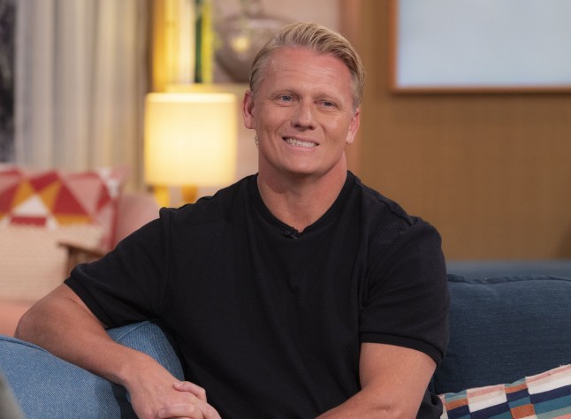 Dr Scott Miller wears a black shirt and sits in the This Morning studio.